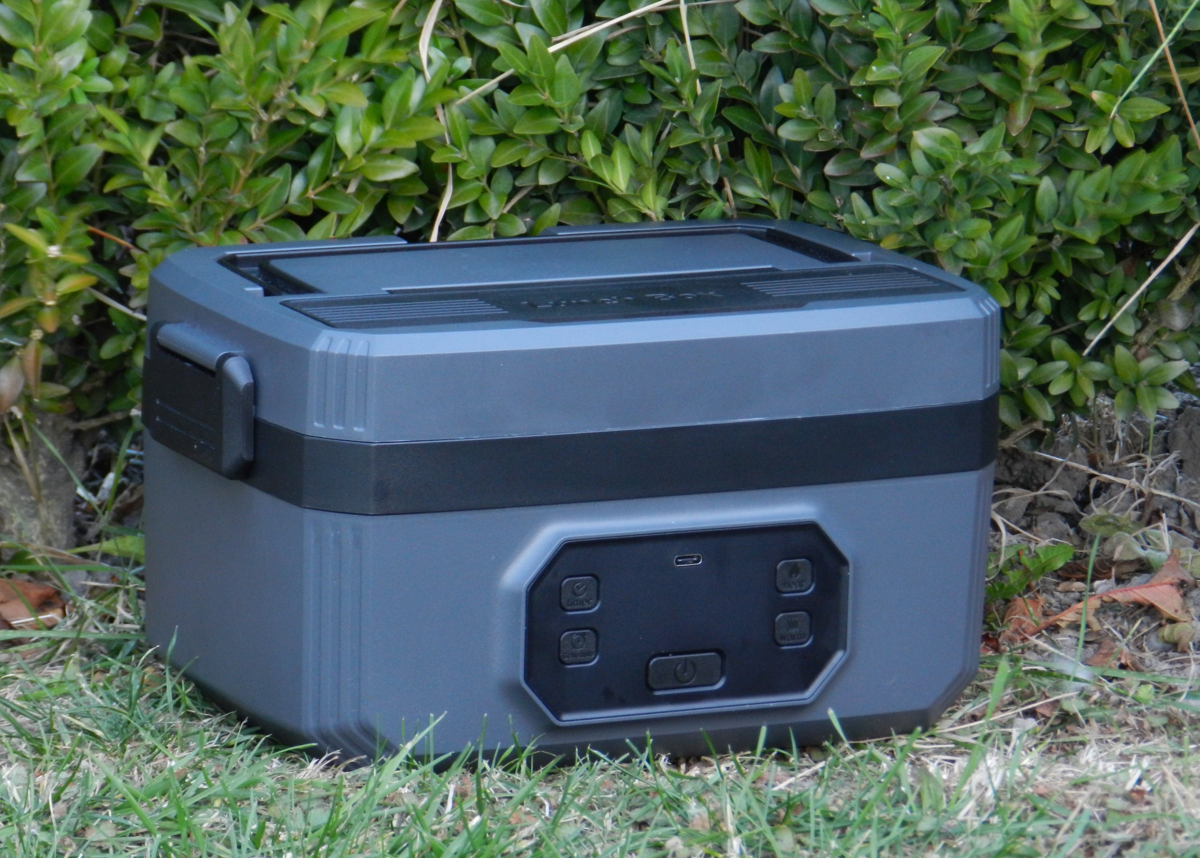 Norva Wireless Heated Lunchbox with a leafy bush in the background.